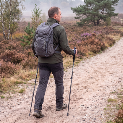 Wandelaar met rugzak loopt met opvouwbare wandelstokken over een zandpad op de heide