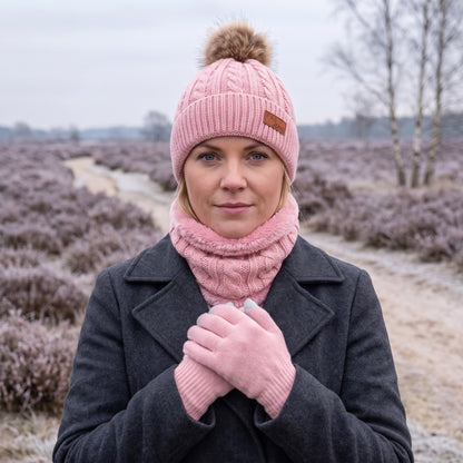 Vrouw met roze wintermuts dames met pompon, bijpassende nekwarmer en touchscreen-handschoenen op een winterse heide